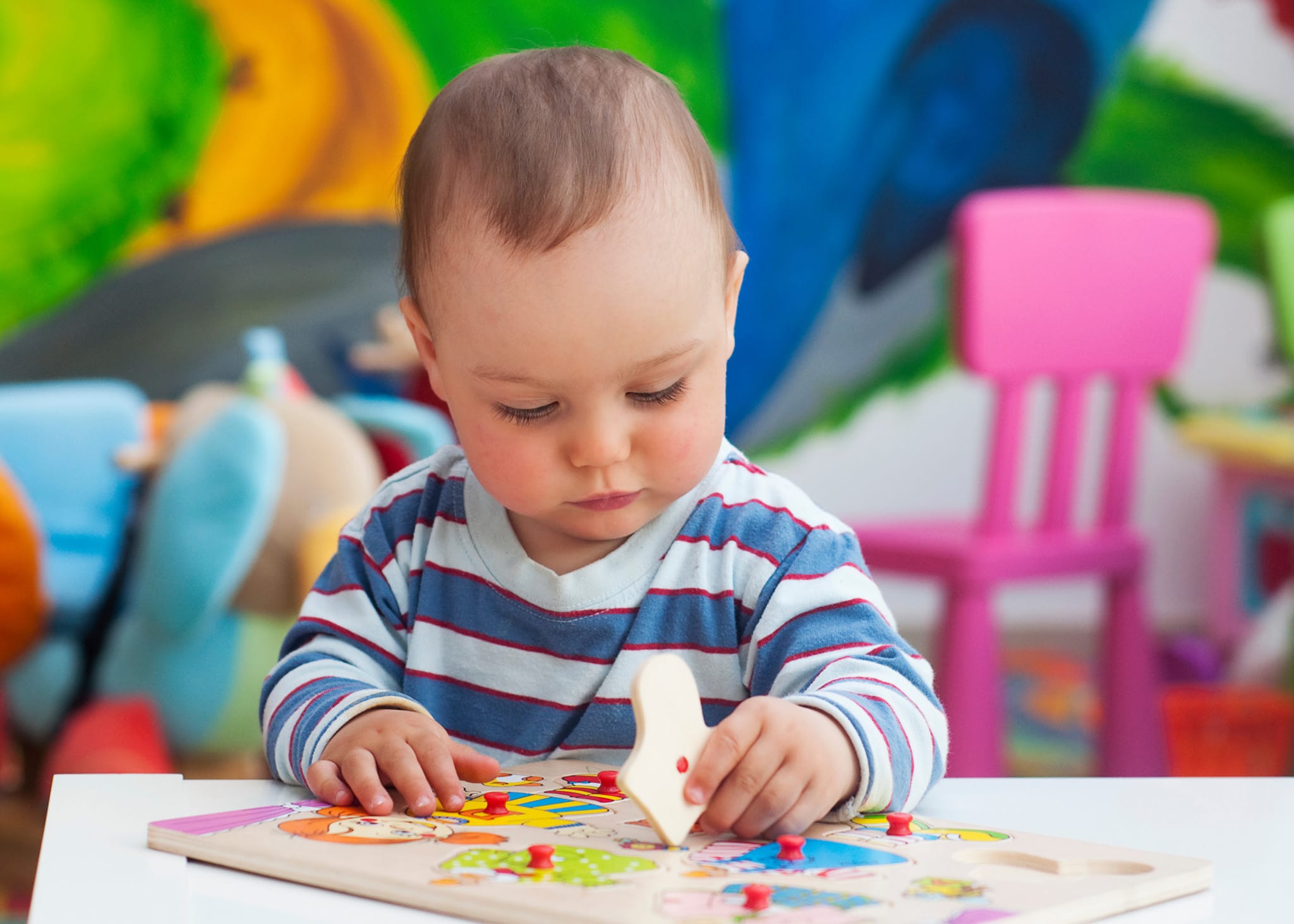 An infant explores problem-solving at a nursery and early childhood centre, developing fine motor skills with a wooden puzzle.